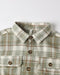A close-up of a plaid button-down shirt with a pointed collar, brown buttons, and two chest pockets on a light gray background.