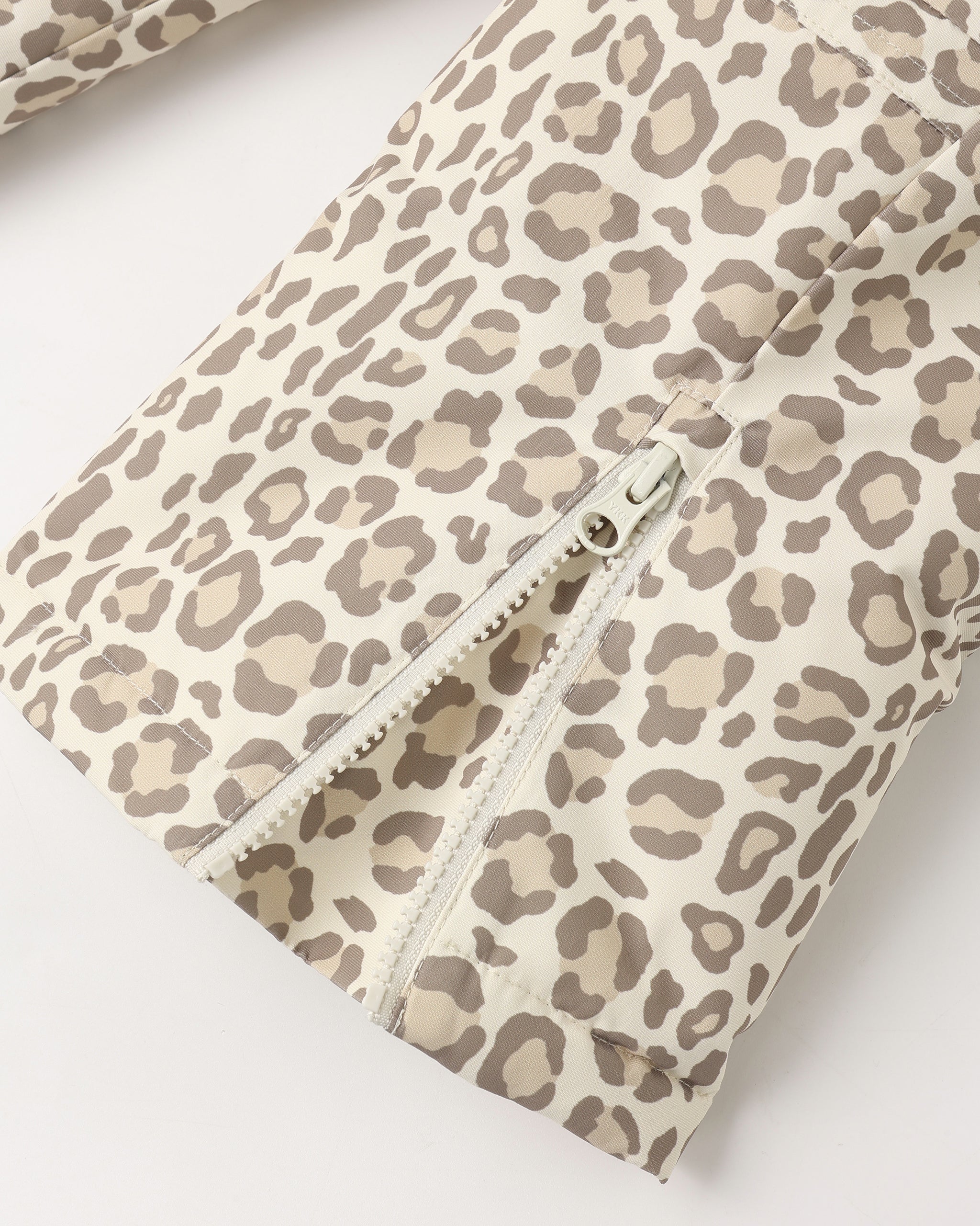 Close-up of a leopard print fabric with a silver zipper, showing a beige and brown animal pattern on a light background.