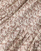 A close-up of a draped fabric with a repeating brown floral and leaf pattern on a warm cream background.