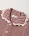 Close-up of a knitted cardigan in dusty mauve pink with a cream scalloped collar and light buttons, showing a brand label that reads 'Ryōn's Cream Sweaters'.