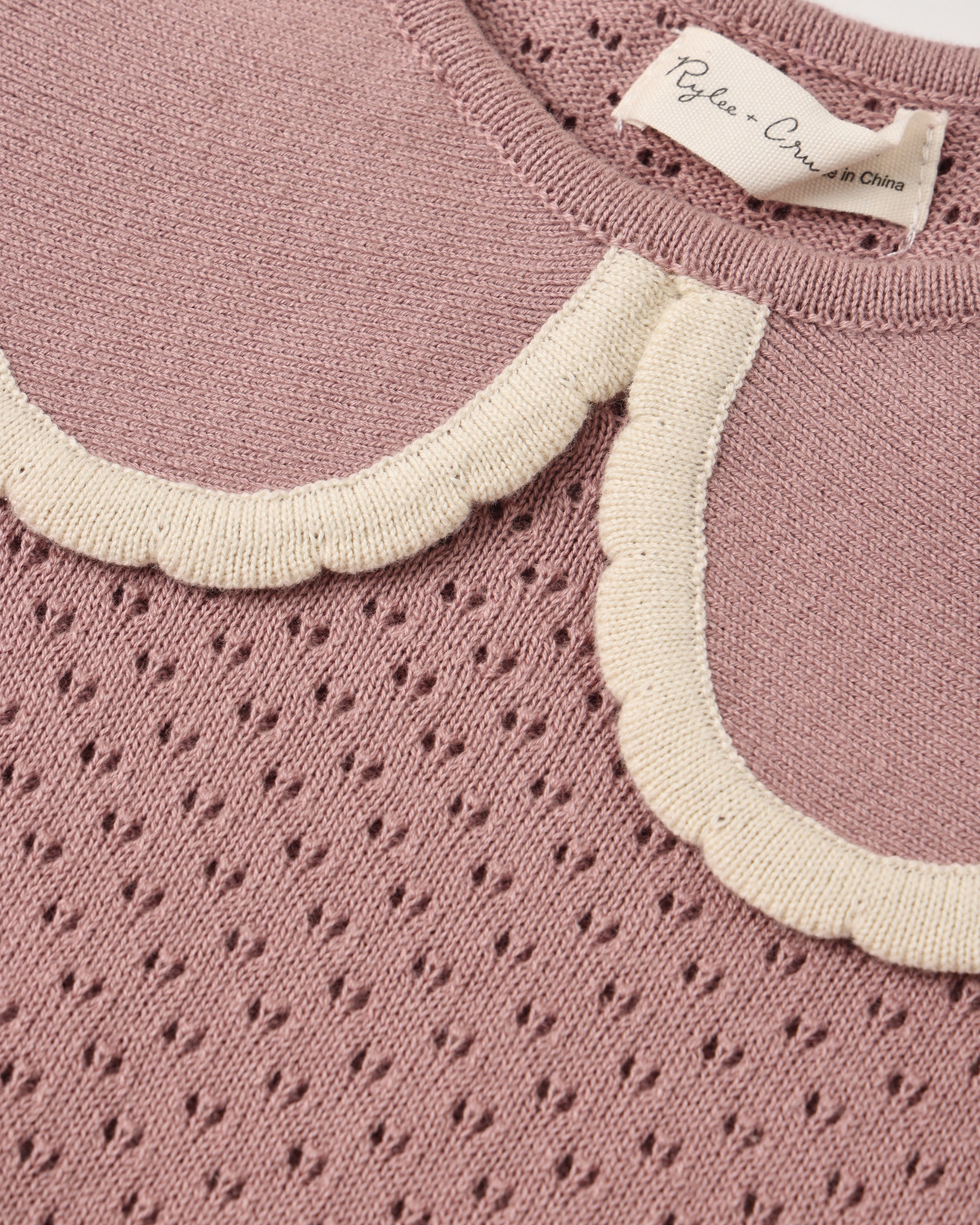 Close-up of a dusty pink knit sweater with a scalloped cream collar and a visible neck label reading 'Pylea - Copenhagen'.