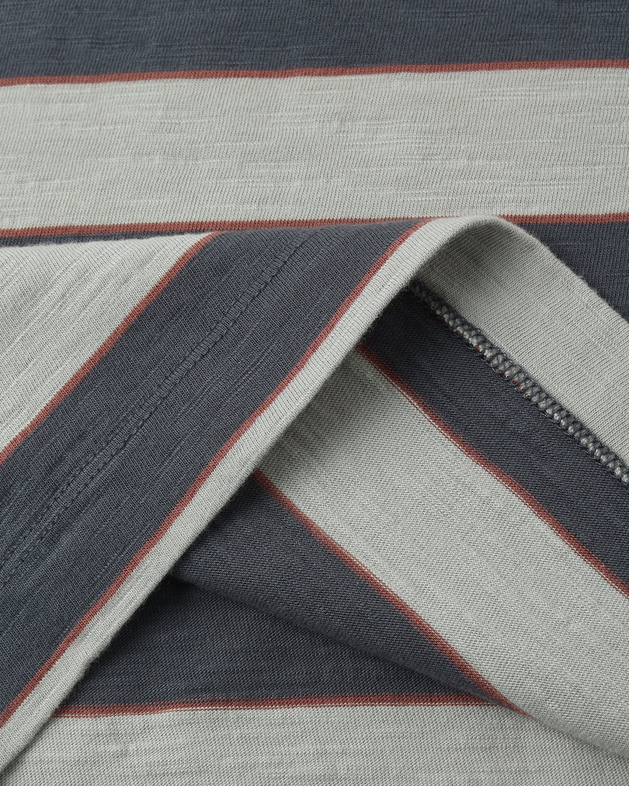 A close-up of a striped textile, likely a blanket or rug, featuring alternating wide stripes of dark slate blue-gray and light gray, separated by thin reddish-brown lines.