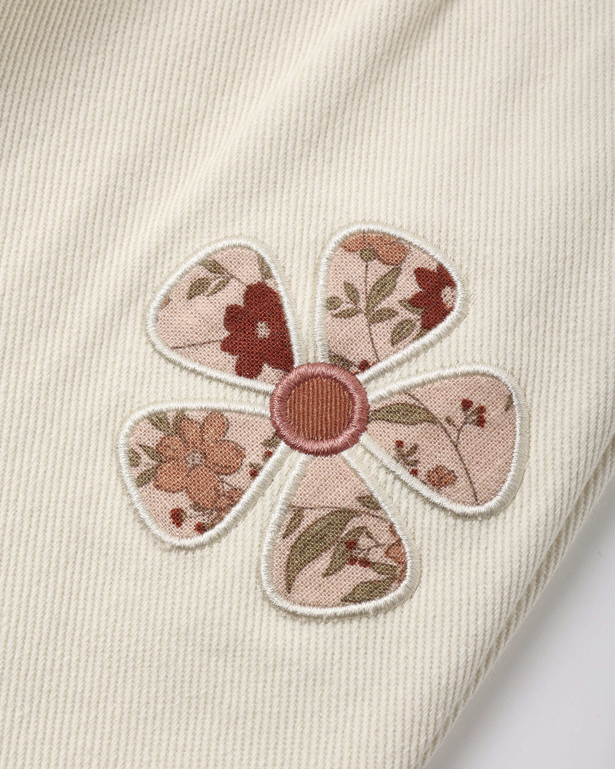 A close up of the daisy patches on a  natural colored denim overall shown  on a white background.