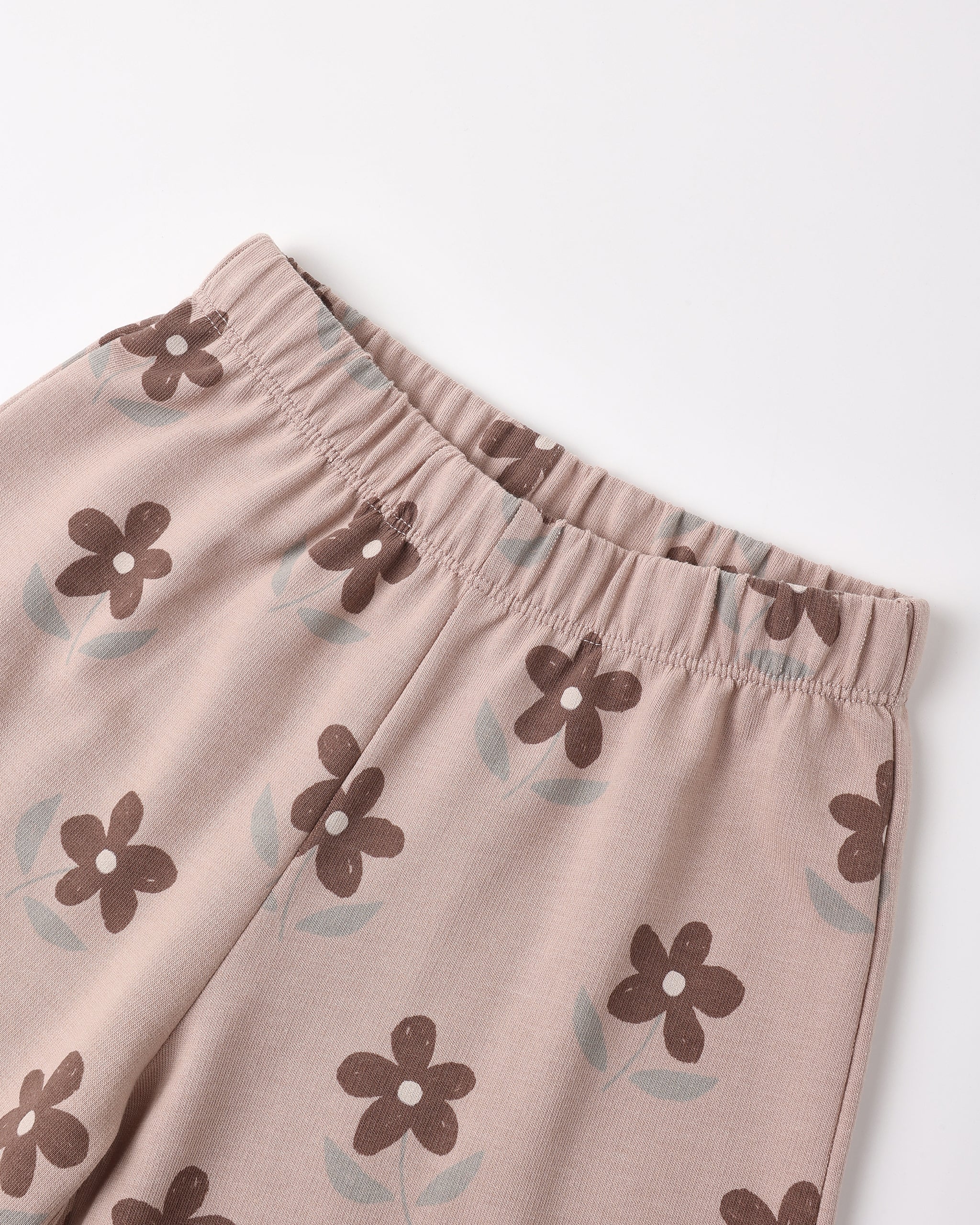 Close-up of a pair of light pink pants with an elastic waistband, featuring an all-over print of brown flowers with light blue-green leaves, shown on a plain white background.