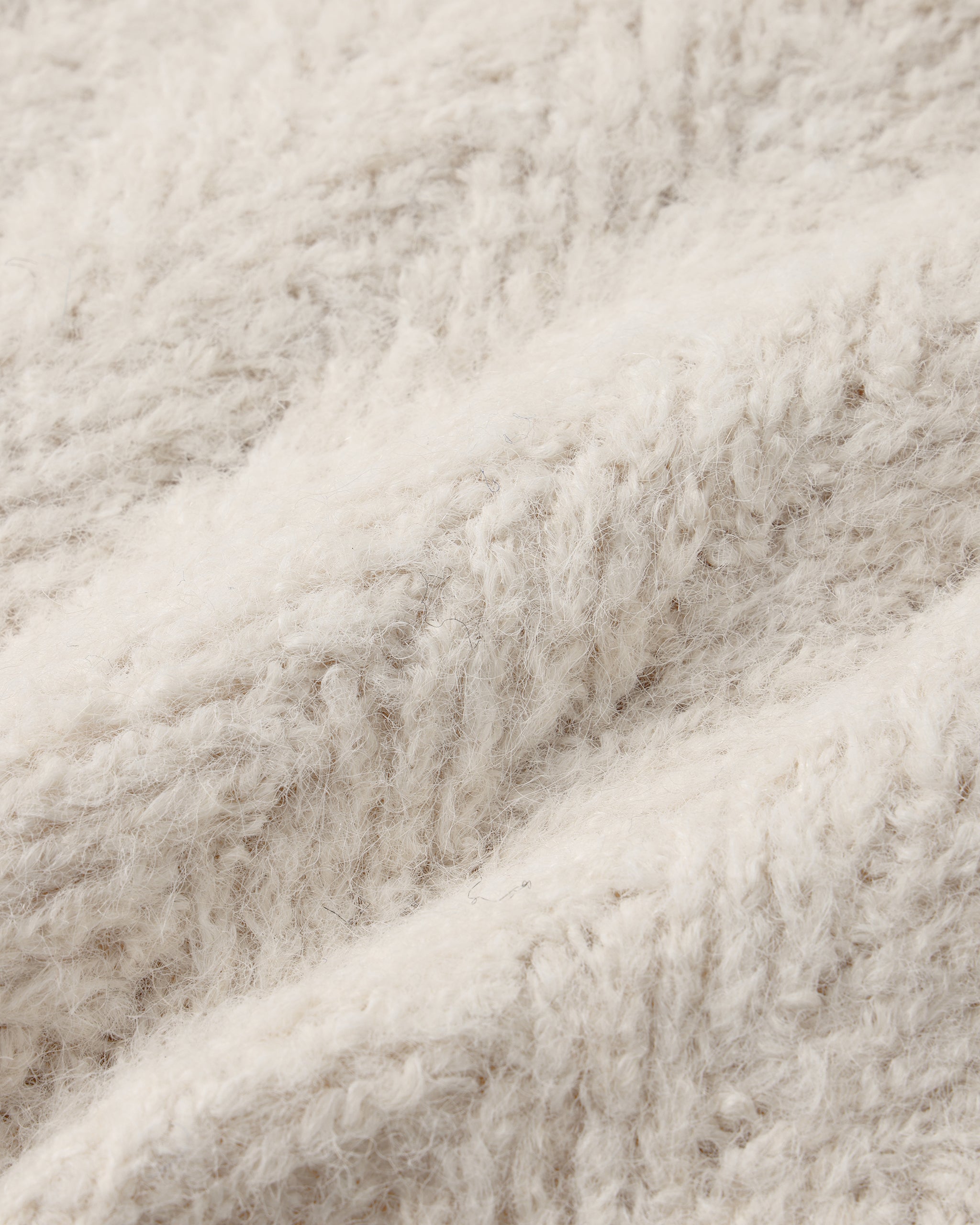 A close-up of a soft, fluffy textured fabric in a warm off-white or cream color, showing the detailed looped pile and folds.