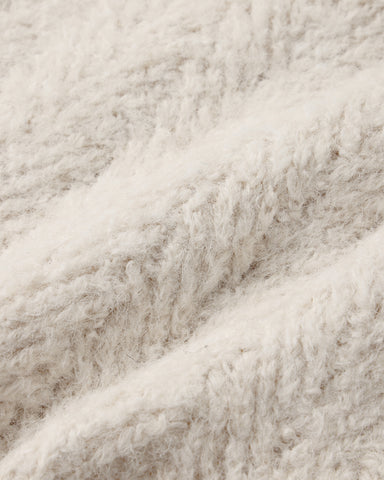 A close-up of a soft, fluffy textured fabric in a warm off-white or cream color, showing the detailed looped pile and folds.