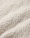 A close-up of a soft, fluffy textured fabric in a warm off-white or cream color, showing the detailed looped pile and folds.