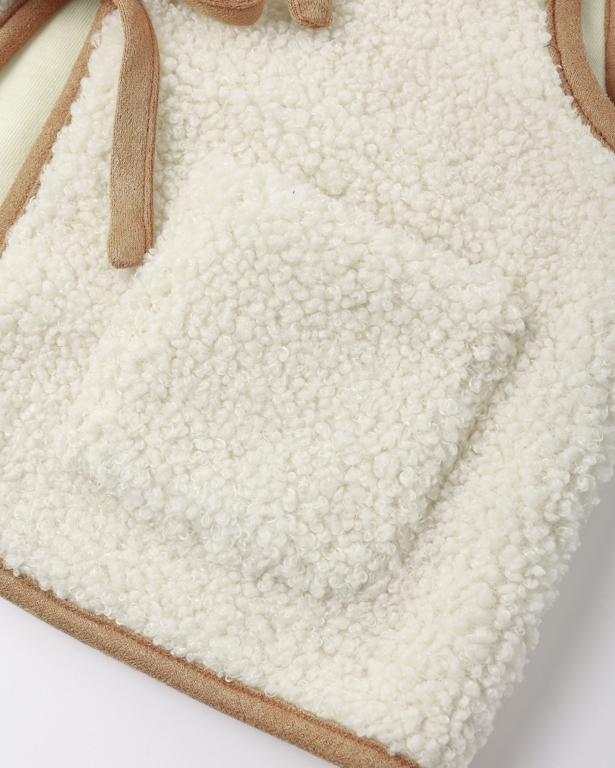 Close-up of a cream sherpa fleece bag with tan suede trim and strap details, showing the soft texture and pocket construction.