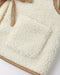 Close-up of a cream sherpa fleece bag with tan suede trim and strap details, showing the soft texture and pocket construction.