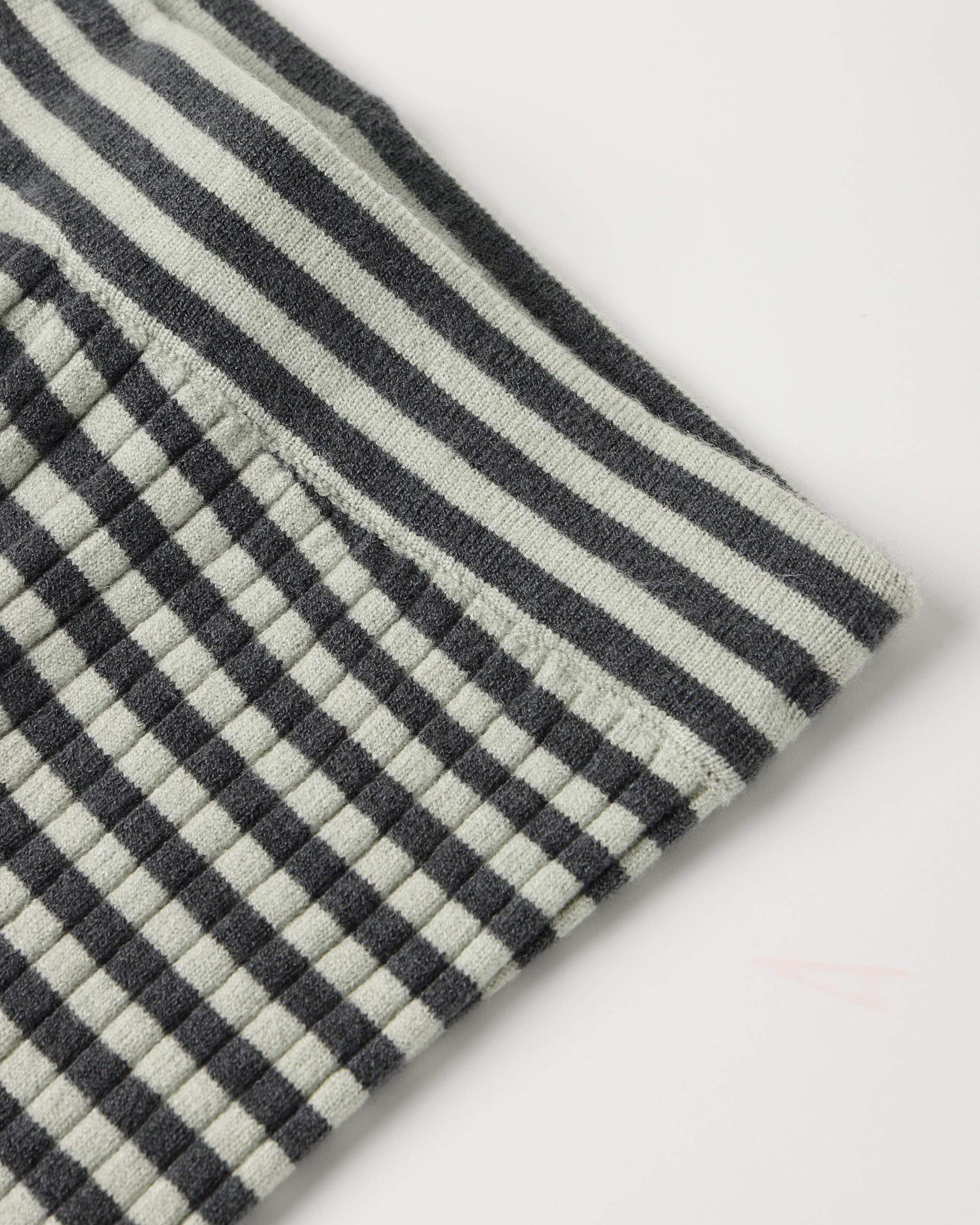 Close-up of a textured fabric with a black and off-white striped pattern and a small stitched pocket on the side, shown on a plain light background.