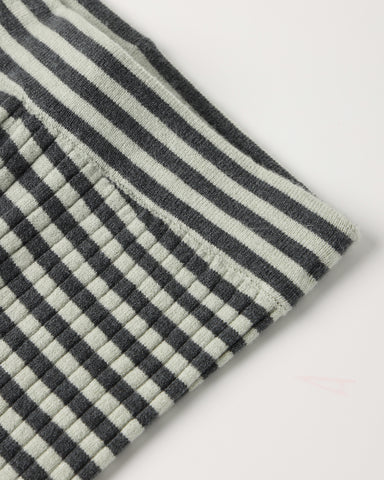 Close-up of a textured fabric with a black and off-white striped pattern and a small stitched pocket on the side, shown on a plain light background.