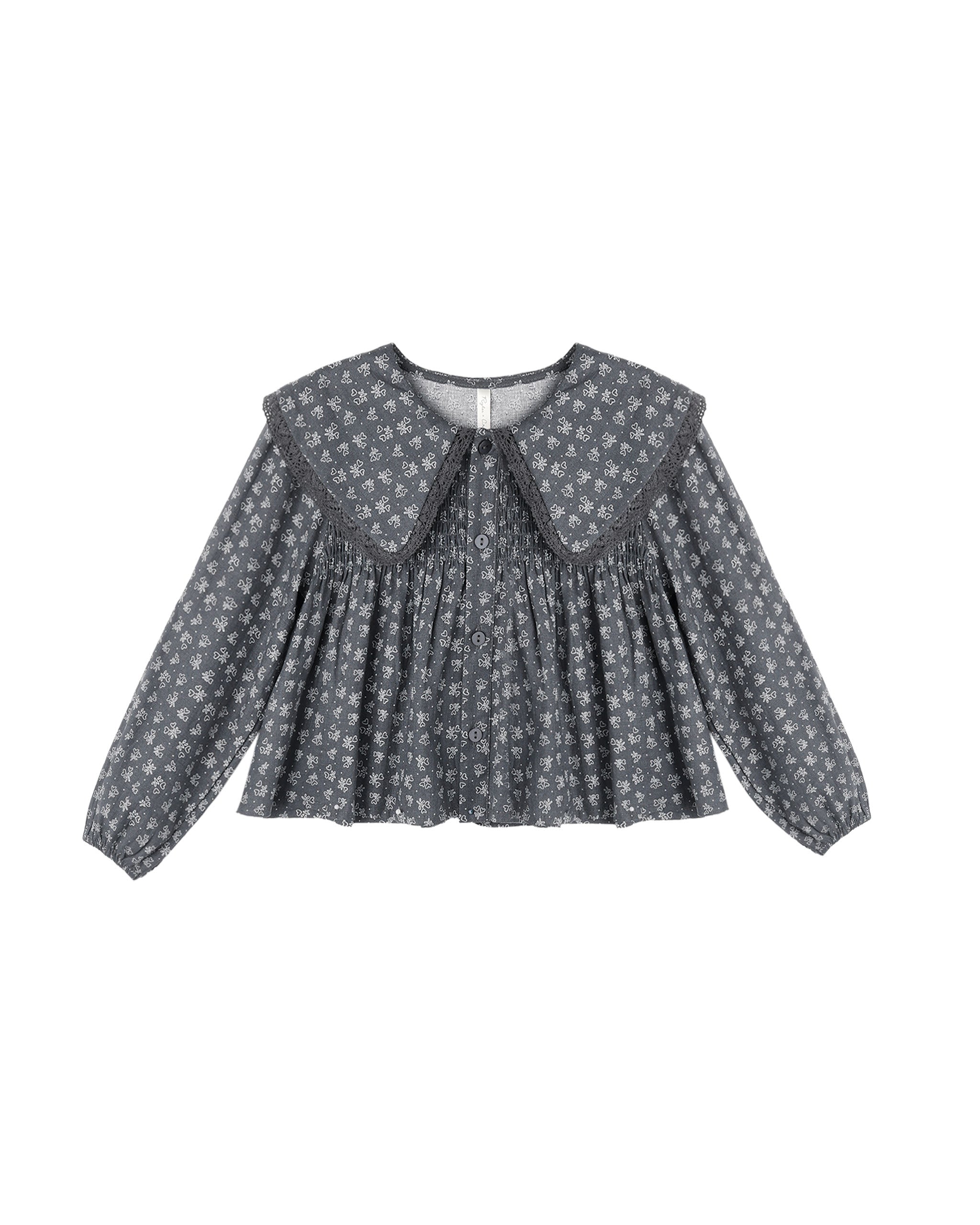 A long-sleeve children's blouse with a dark gray and white floral pattern, featuring a large Peter Pan collar and a smocked bodice, shown against a plain white background.
