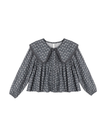 A long-sleeve children's blouse with a dark gray and white floral pattern, featuring a large Peter Pan collar and a smocked bodice, shown against a plain white background.