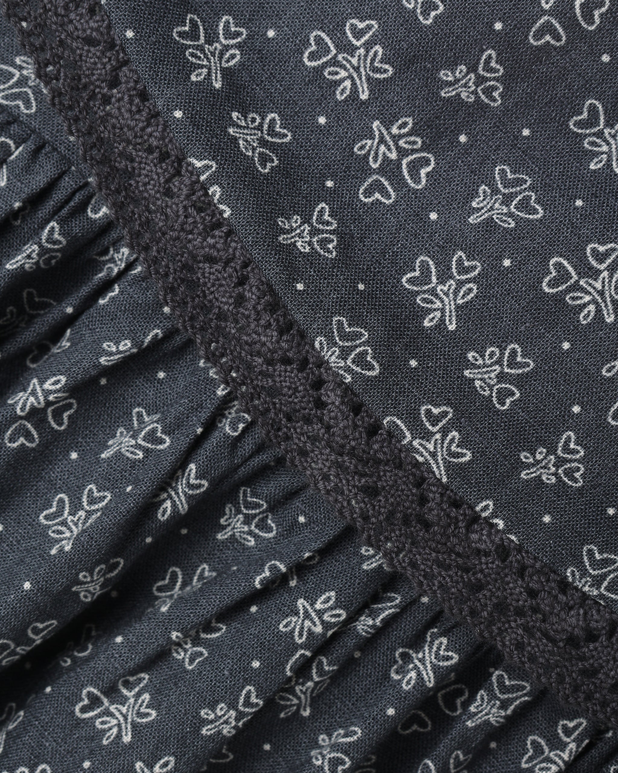 Close-up of a dark gray fabric with a white outline floral and heart pattern, featuring a ruffled trim along the edge.