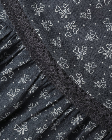 Close-up of a dark gray fabric with a white outline floral and heart pattern, featuring a ruffled trim along the edge.