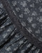 Close-up of a dark gray fabric with a white outline floral and heart pattern, featuring a ruffled trim along the edge.