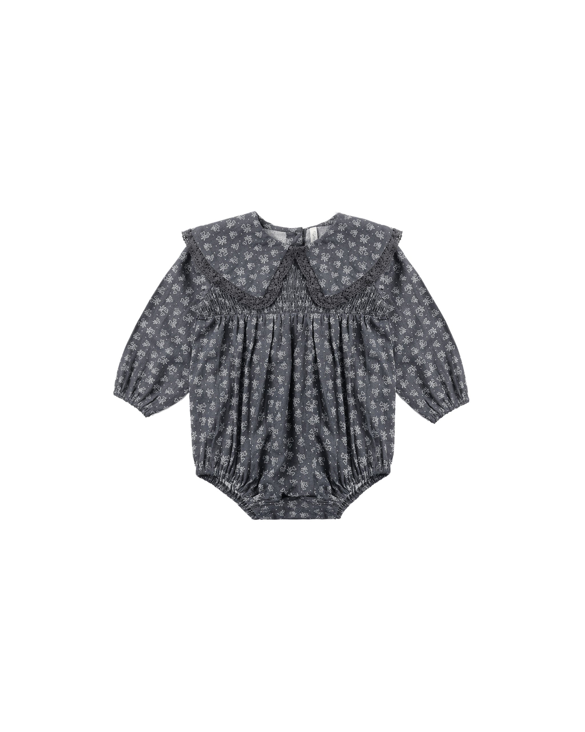A baby girl's long-sleeve romper in a dark blue and white floral print, featuring a wide ruffled Peter Pan collar and a smocked bodice, shown flat on a white background.