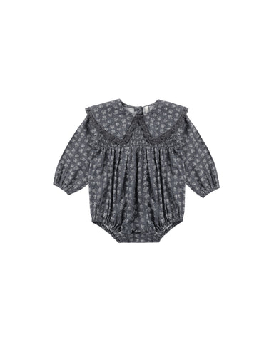 A baby girl's long-sleeve romper in a dark blue and white floral print, featuring a wide ruffled Peter Pan collar and a smocked bodice, shown flat on a white background.