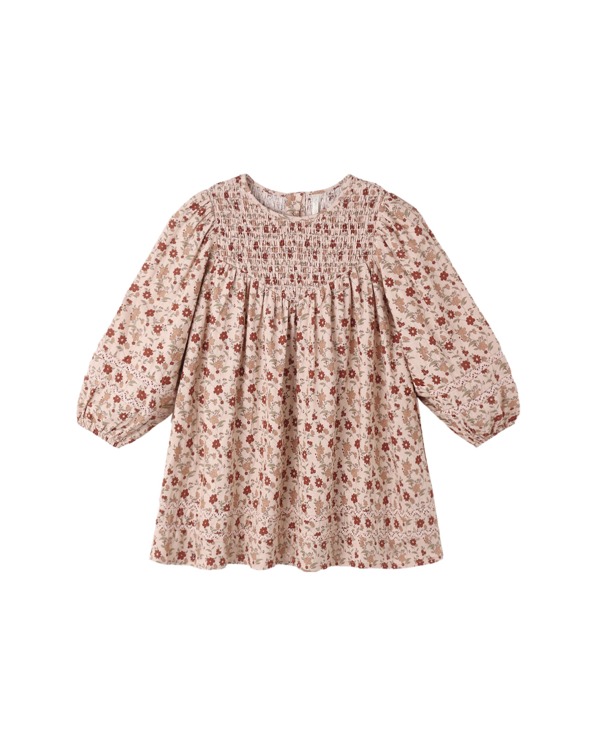 A blush colored dress with a floral pattern featuring a smocked front bodice, puff sleeves with encased elastic cuffs, and delicate crochet lace inlay