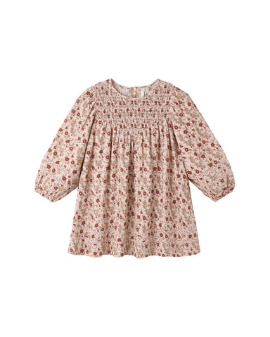 A blush colored dress with a floral pattern featuring a smocked front bodice, puff sleeves with encased elastic cuffs, and delicate crochet lace inlay