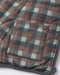 Close-up of a quilted puffer jacket with a muted plaid pattern in dusty rose, gray, and off-white, featuring a zippered pocket and dark gray trim.