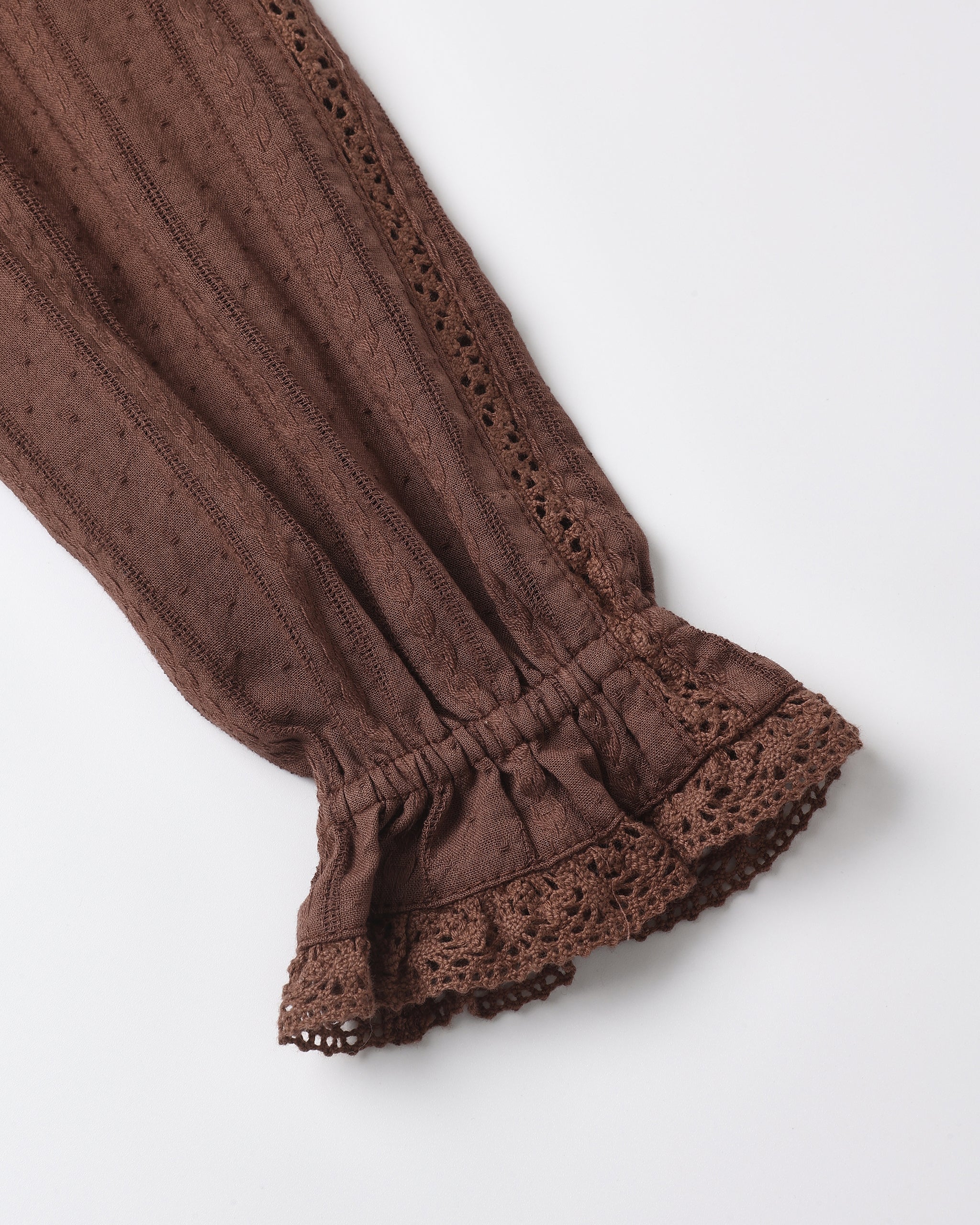 A close-up of a brown textured fabric sleeve with a gathered elastic cuff and decorative lace trim, shown on a plain light background.