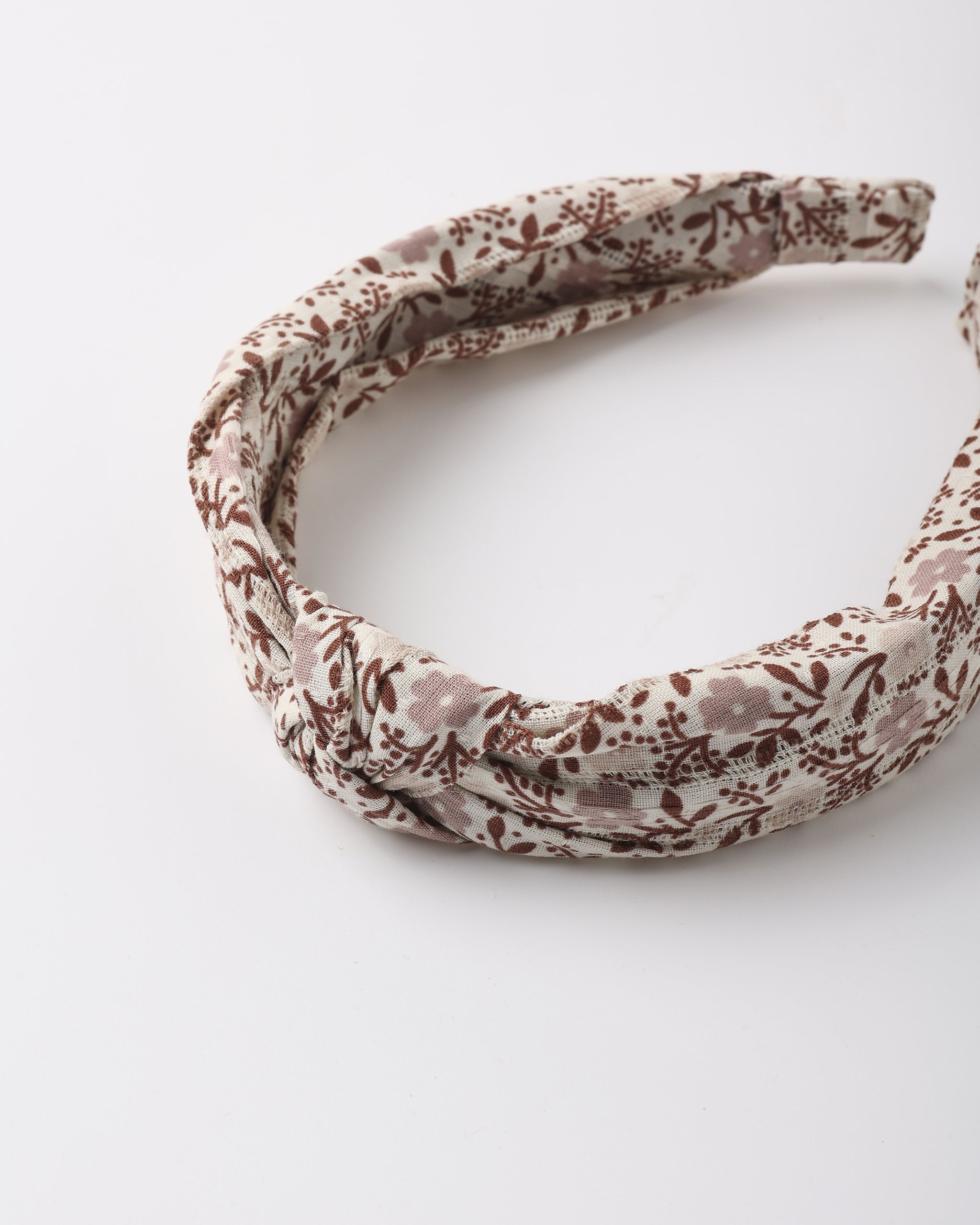 A twisted fabric headband with a brown floral and botanical pattern on a light beige background, photographed on a clean white surface.