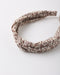 A twisted fabric headband with a brown floral and botanical pattern on a light beige background, photographed on a clean white surface.