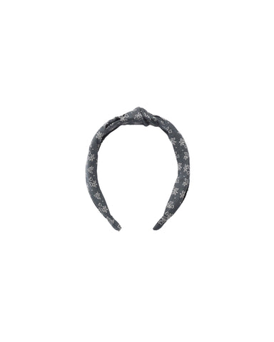 A dark gray fabric headband with a white floral pattern, featuring a knotted top detail, shown against a plain white background.