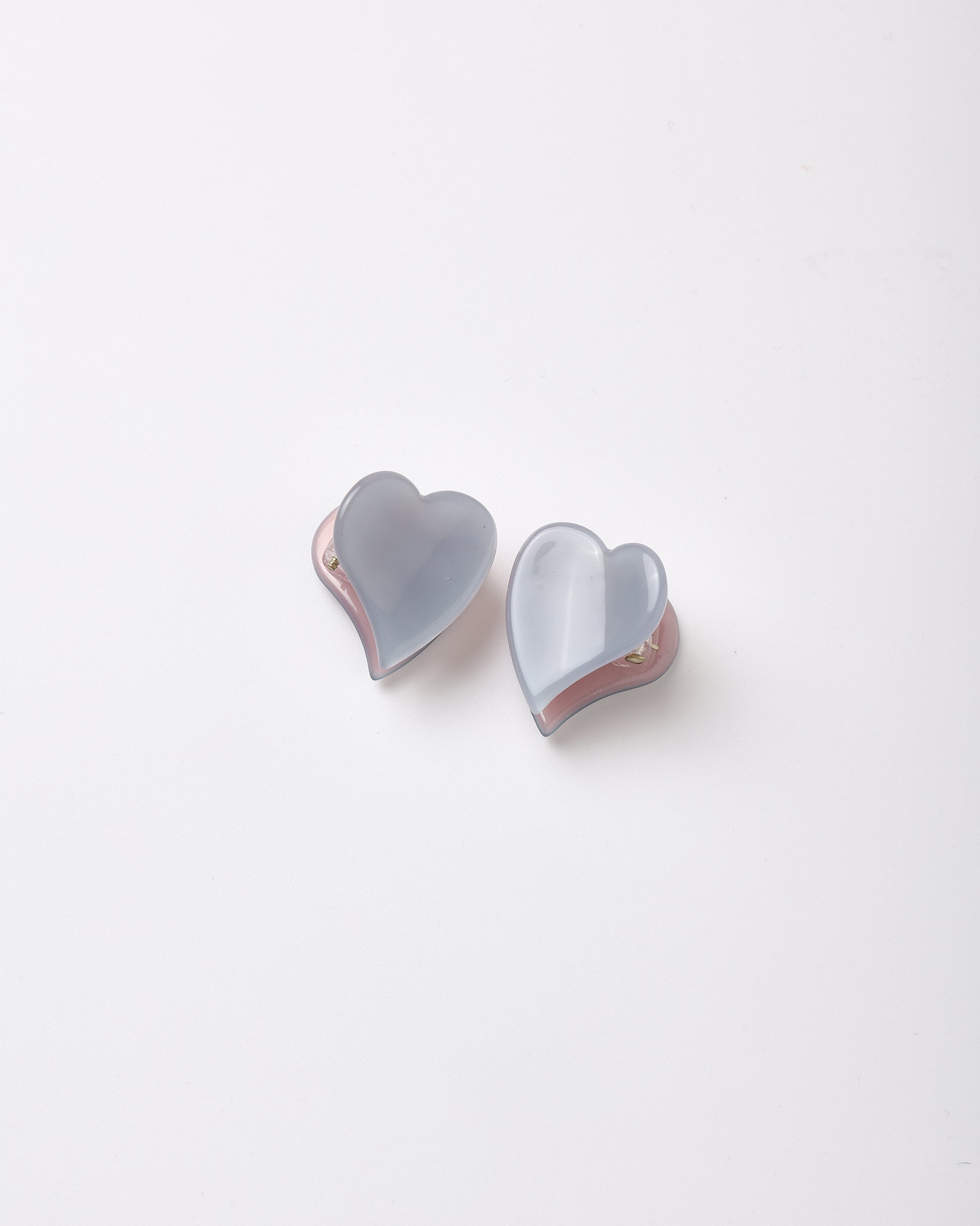 A pair of heart-shaped stud earrings with a translucent light blue-gray resin front and a pink inner lining, shown on a plain white background.