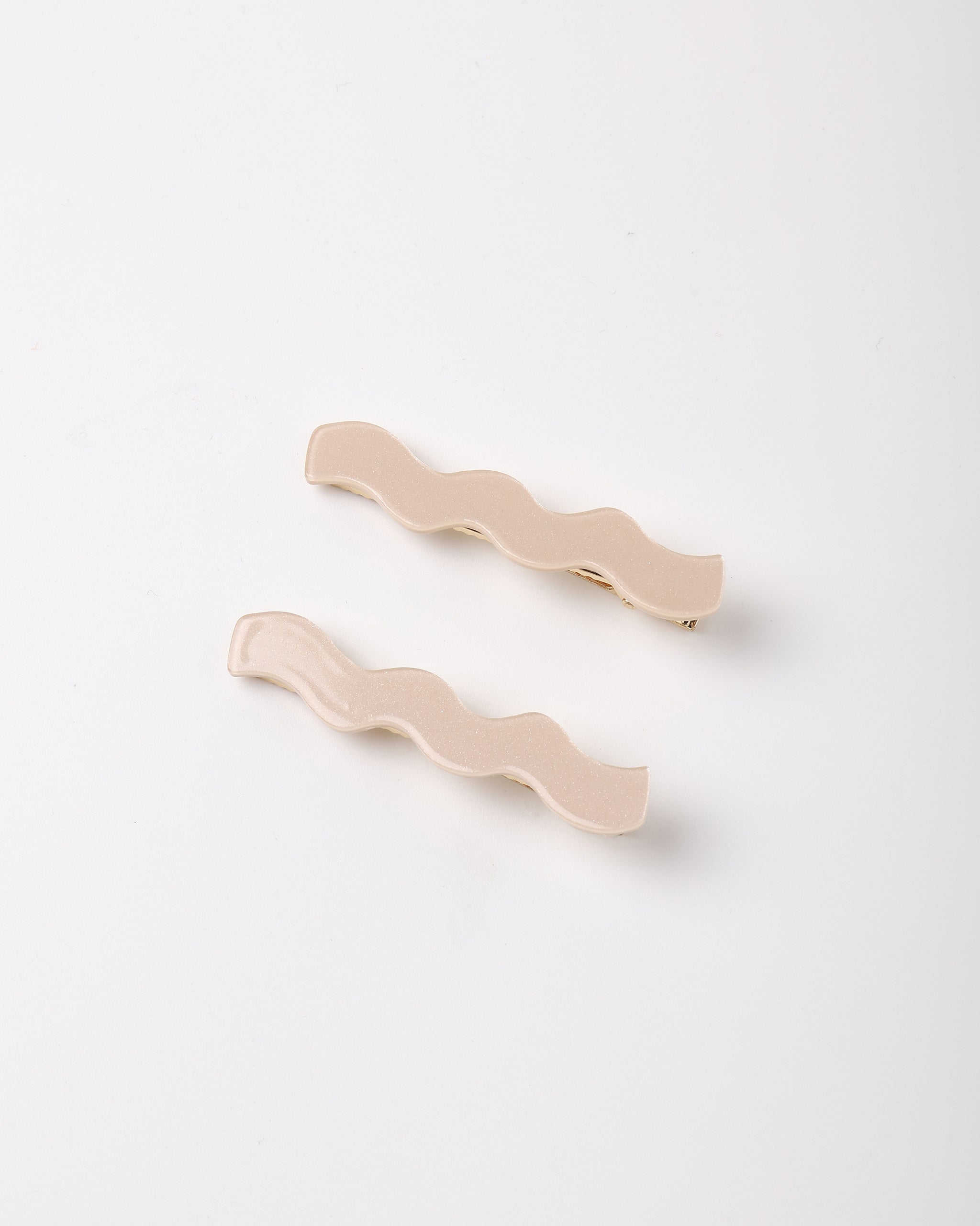 Two wavy hair clips in a light beige color, arranged diagonally on a clean white background.