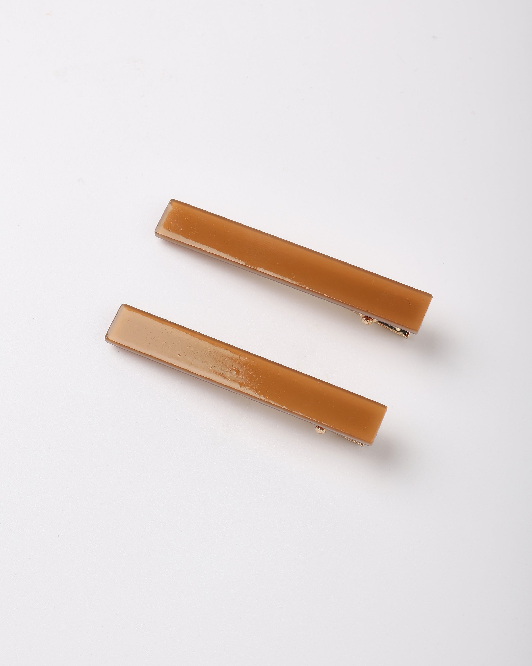 Two rectangular hair claw clips in a warm caramel brown translucent resin, displayed diagonally on a clean white background.