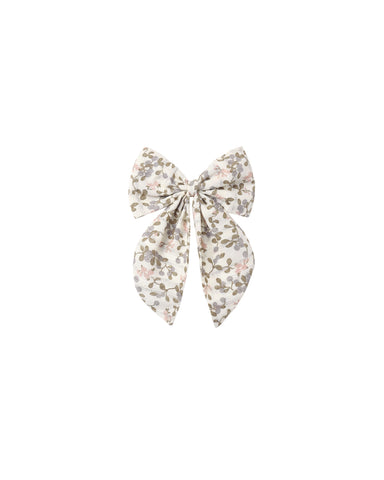 A fabric hair bow with a delicate floral print in muted pink, olive green, and gray on a cream background, centered on a solid white background.
