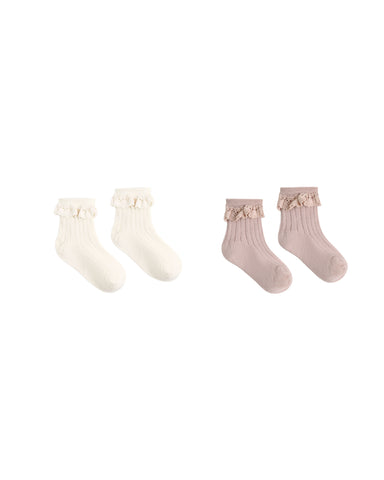 Two pairs of ribbed baby socks with ruffled trim, shown on a plain white background. One pair is off-white/cream and the other is dusty pink, both with small bow details at the top.