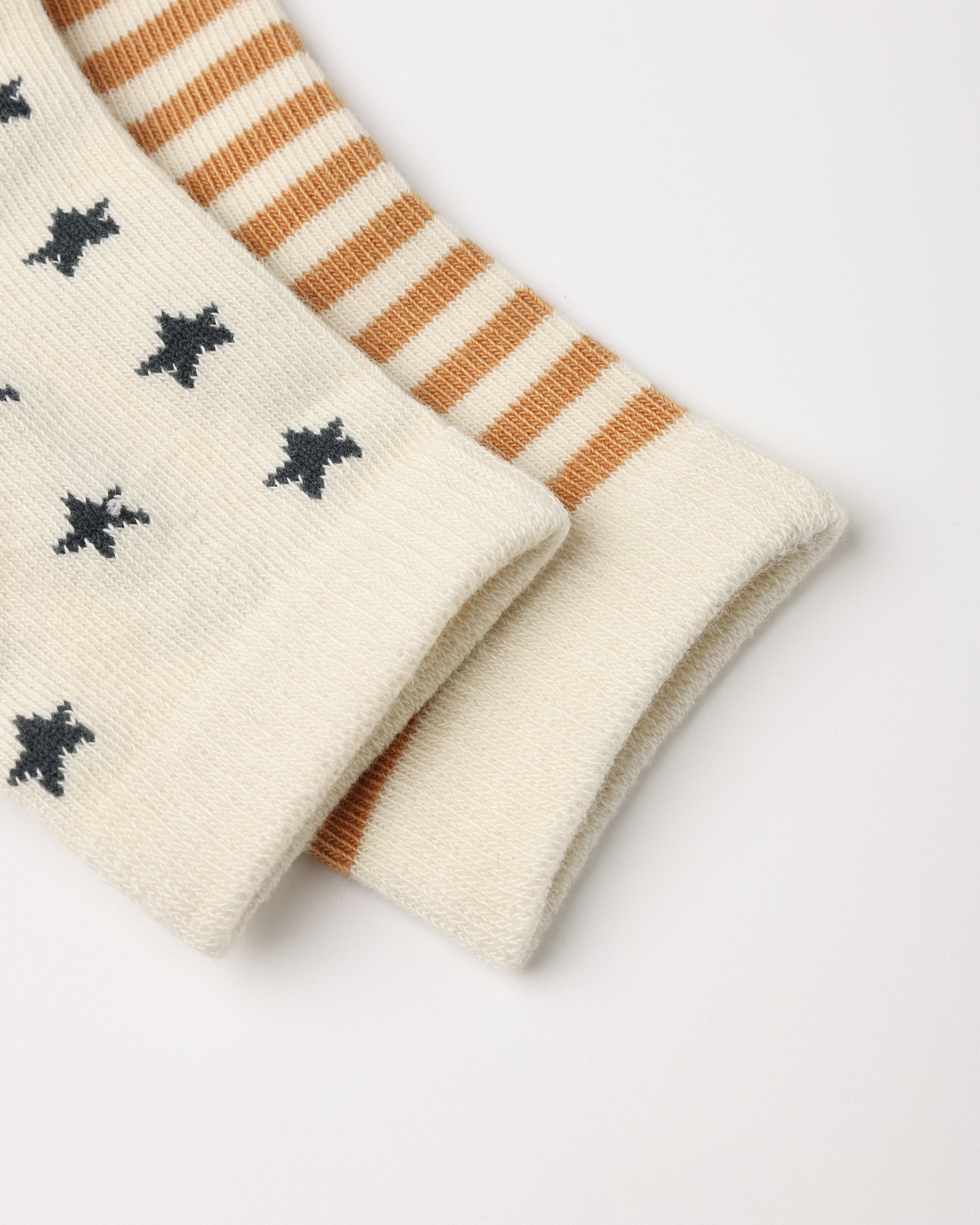 Close-up of a pair of cream knit socks folded on a white background. One sock has small dark gray star-like motifs, and the other has alternating cream and tan stripes.