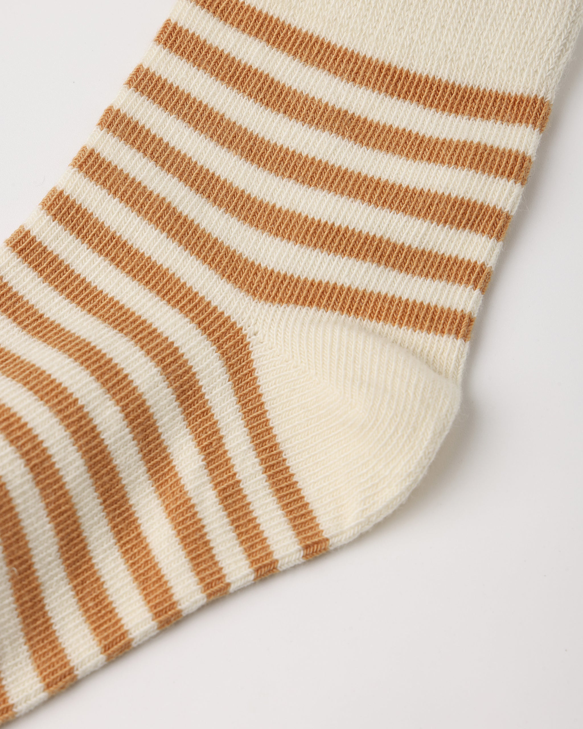 A close-up of a striped sock with alternating warm brown and cream horizontal stripes, showing the ribbed knit texture and the toe area on a light gray background.