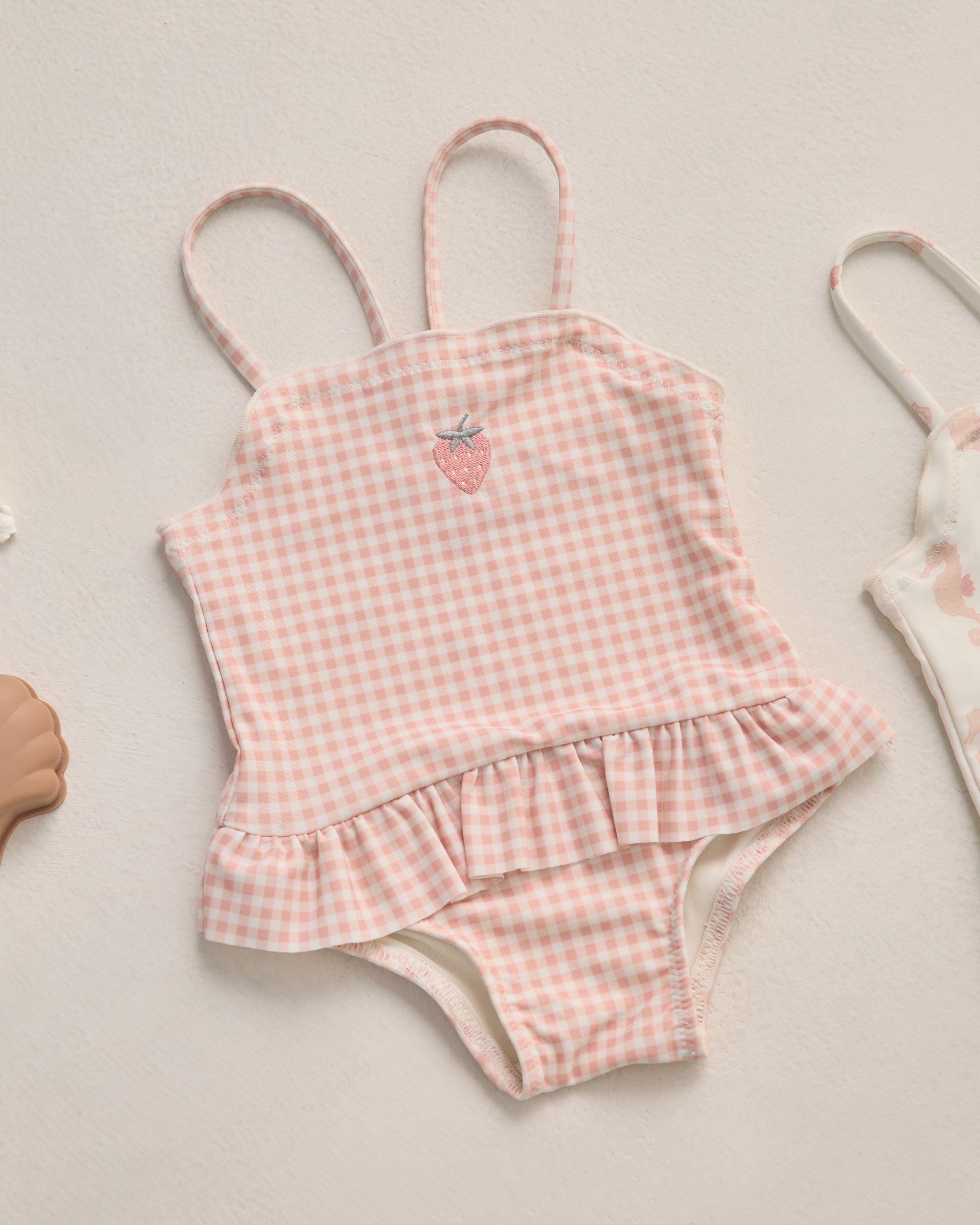 Pink gingham swimsuit with ruffle details on a light background