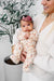 Woman holding a baby in a floral outfit with a plant in the background