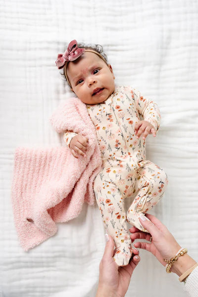 Baby in floral outfit with pink blanket on white surface