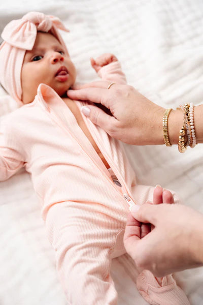 Baby wrapped in a pink striped zipper footie with a headband, being held by a person on a white background