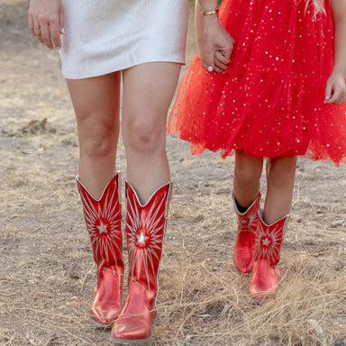 Two people wearing red cowboy boots with star patterns on a dry grass background.