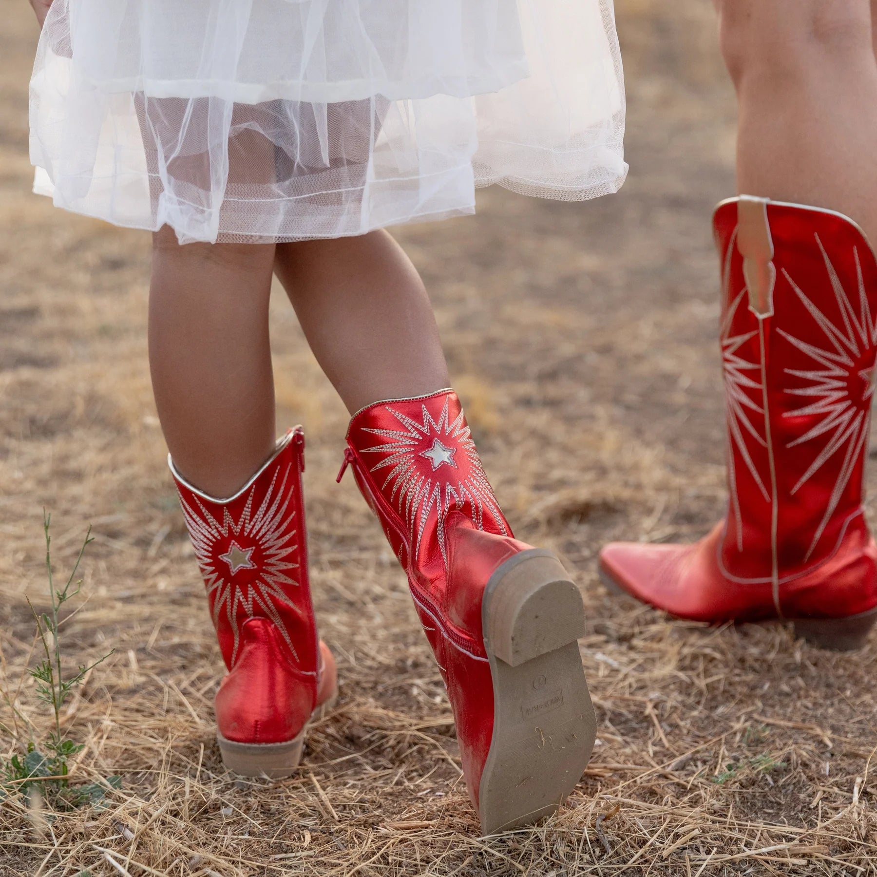 Red cowboy boots with white star patterns worn by children in a field.