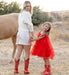 Woman and young girl in red cowboy boots standing next to a horse in a natural setting.