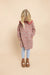 A young girl with blonde hair is wearing a long-sleeved dress with a red, white, and blue floral pattern, light blue leggings, and brown boots, standing against a solid beige background.