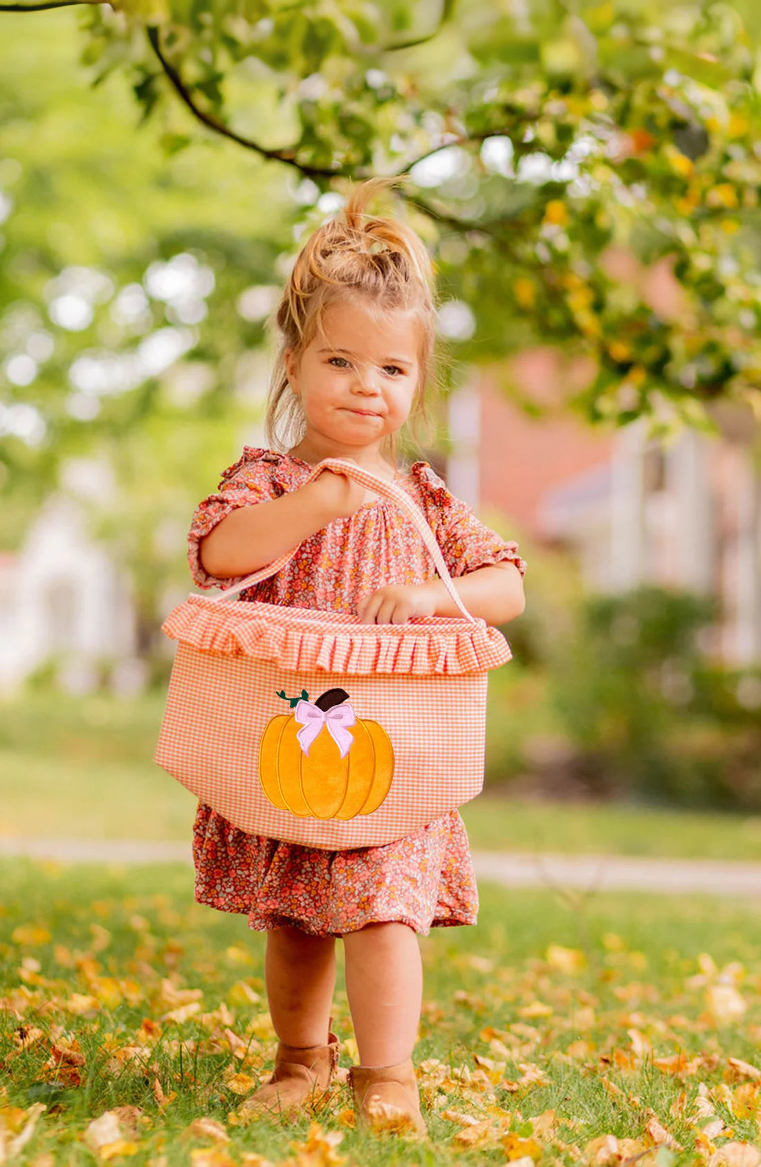 Young girl in a pink dress with a pumpkin bag outdoors