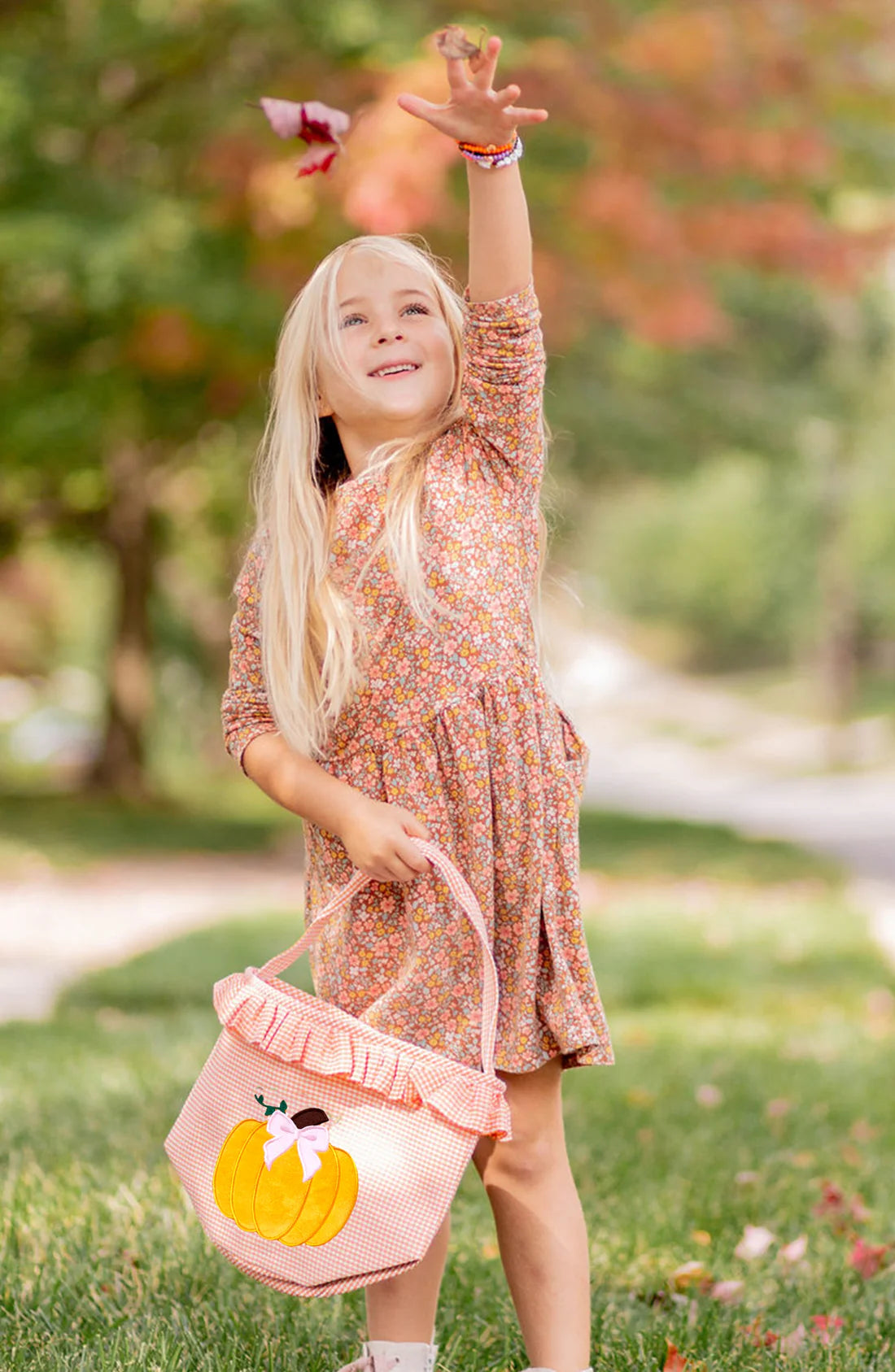 Young girl in a floral dress holding a pink bag with a duck design in an outdoor setting.