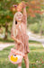 Young girl in a floral dress holding a pink bag with a duck design in an outdoor setting.
