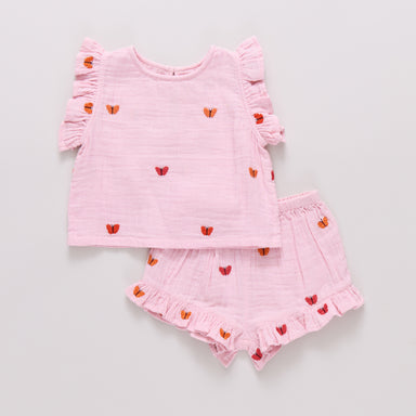 Pink children's outfit with embroidered butterflies and ruffled sleeves and shorts on a light gray background