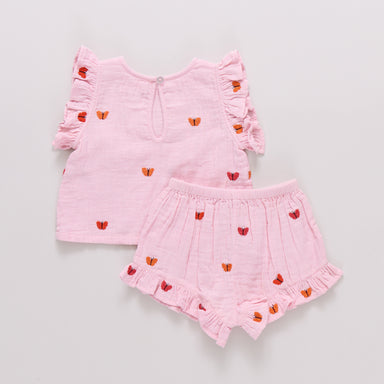 Pink children's outfit with ruffled top and shorts on a light gray background