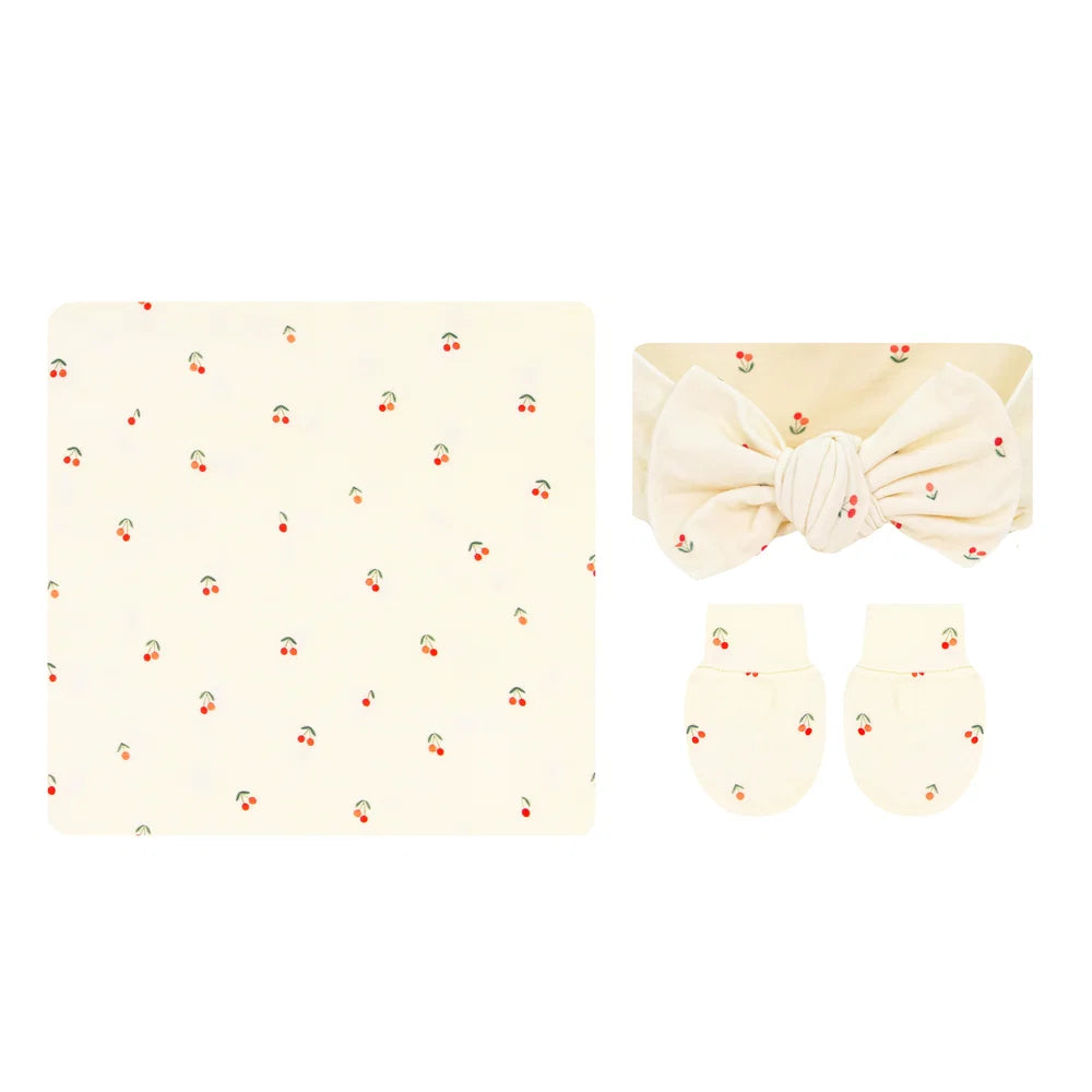 Baby set featuring a cream-colored blanket, a matching headband with a large bow, and a pair of mittens, all decorated with a small cherry print.
